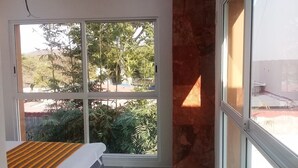 A bedroom with a bed, a large window, and a view of greenery outside. - PALMAS DE CHAHUE 8 (1,100 SF) (Bahías de HUATULCO)