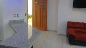 A room with a granite countertop, a wooden door, a red sofa, and a flat-screen TV mounted on the wall. - PALMAS DE CHAHUE 8 (1,100 SF) (Bahías de HUATULCO)