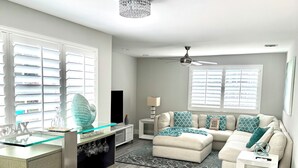 A modern living room with a glass-top kitchen island, a beige sofa set, and a ceiling fan.