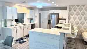 A modern kitchen with white cabinetry, a central island, stainless steel appliances, and a patterned wallpaper design.