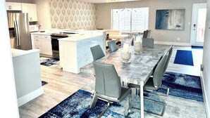 A modern kitchen with white cabinetry, a central island, and a dining area with a marble table and chairs.