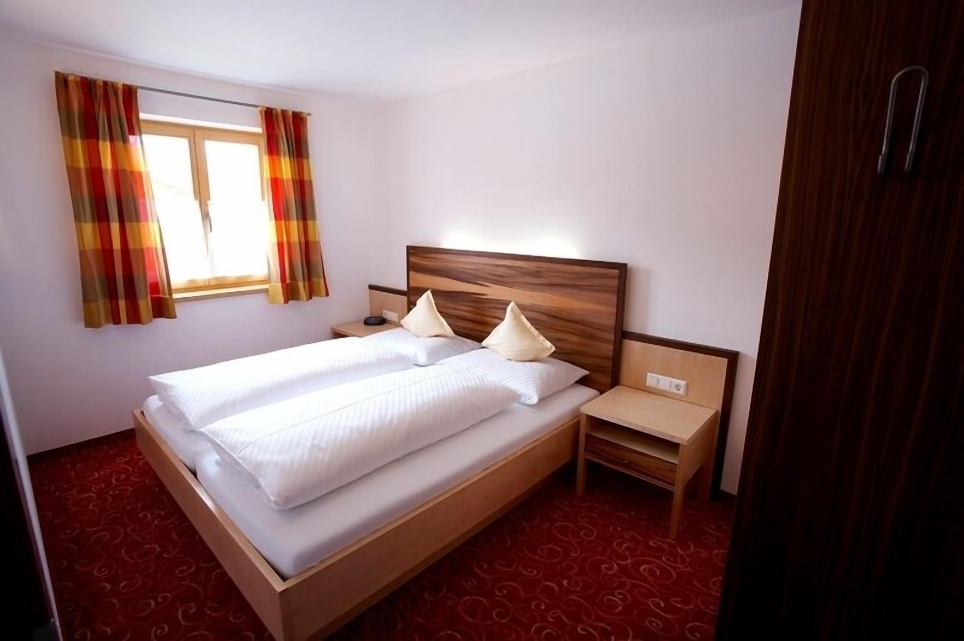 Una habitación de hotel con una cama de madera, dos mesitas de noche y un ventanal con cortinas.