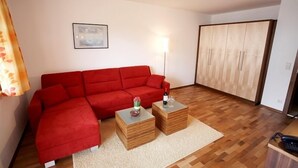 Un salon avec un canapé rouge, deux petites tables en bois, une lampe et une armoire.