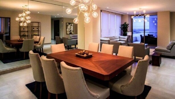 A modern dining area with a wooden table and chairs, a chandelier, and a view of the city at night.