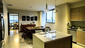 A modern kitchen with a central island, dining area with chairs, and a view through the window.
