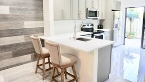 A modern kitchen with a central island, two bar stools, stainless steel appliances, and a view of the outdoors. - : Sandy Feet Retreat: Walk to the Beach! : (Jupiter)