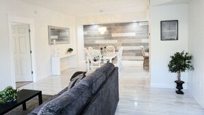 A modern living room with a grey sofa, a dining table with white chairs, and a kitchen area with a grey backsplash. - : Sandy Feet Retreat: Walk to the Beach! : (Jupiter)