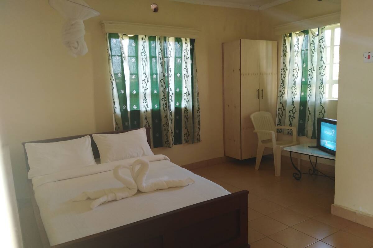 A hotel room with a bed, a desk with a television, a wardrobe, and curtains.