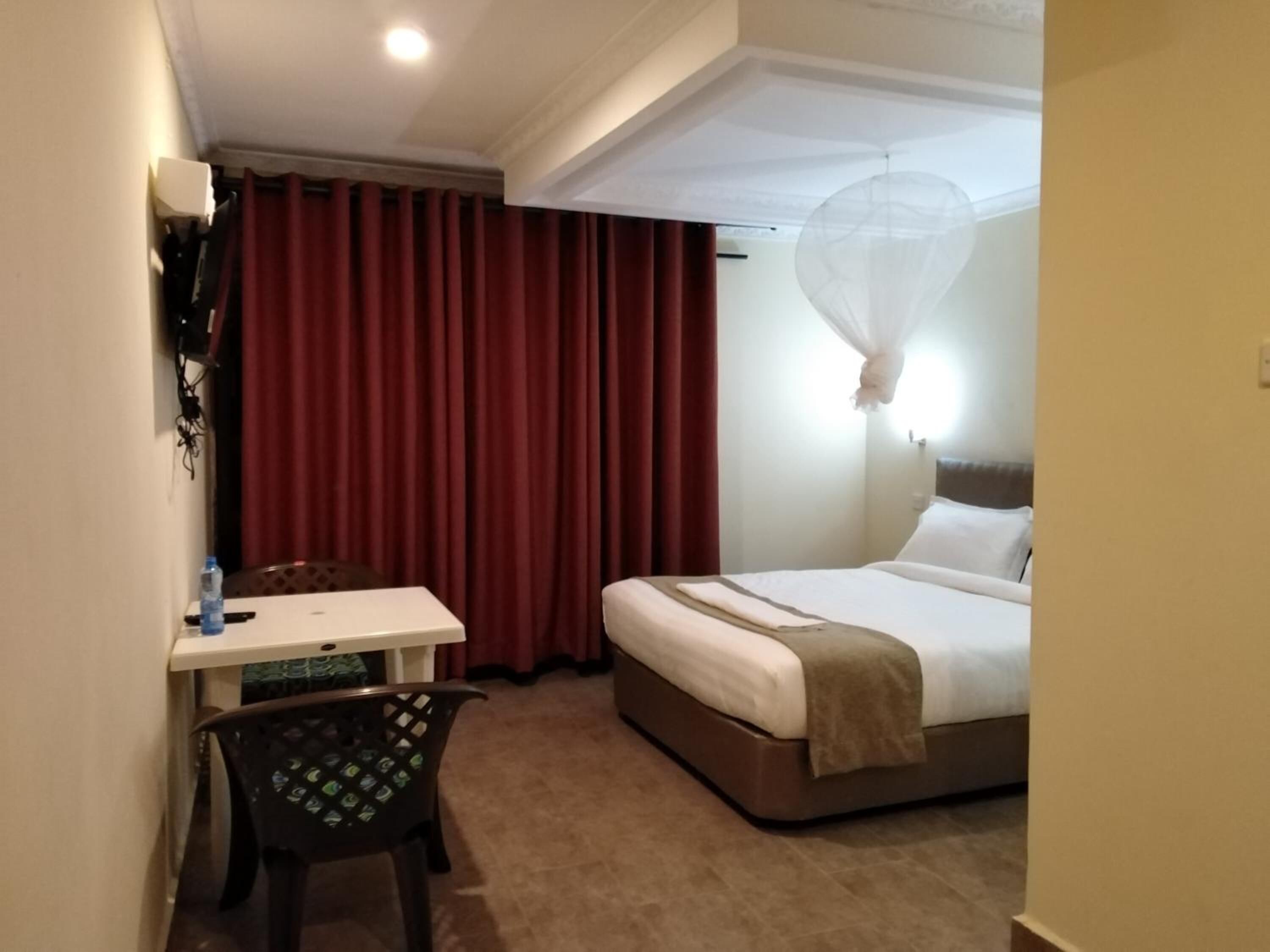 A hotel room with a bed, a desk, a chair, and a curtain.