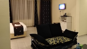 A hotel room with a bed, a sofa, a television, and a minibar. - Lantana Comfy (Kakamega)