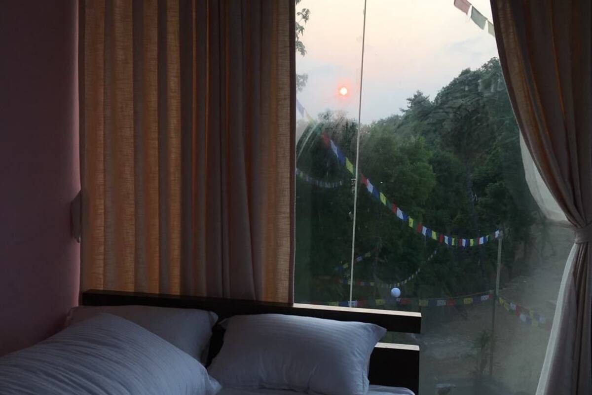 A bedroom with a bed, curtains, and a window with a view of trees and a flag.
