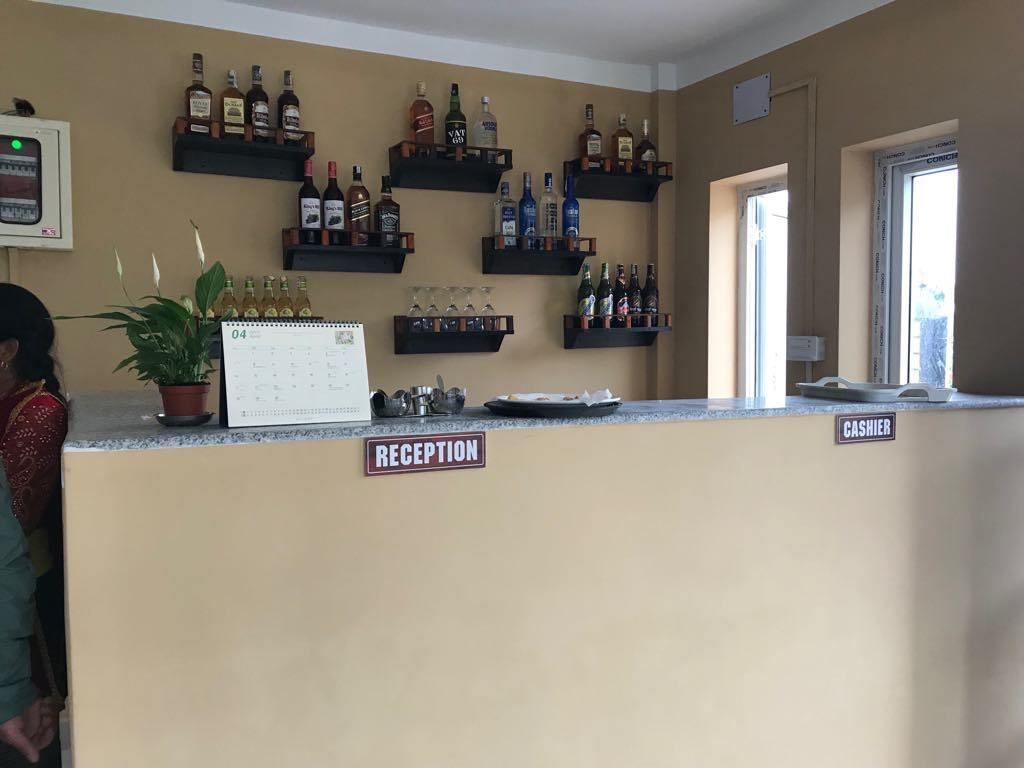 Una zona de recepción con un mostrador color beige, un calendario y estantes llenos de botellas de licor.