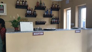 Una zona de recepción con un mostrador color beige, un calendario y estantes llenos de botellas de licor.