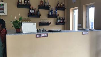 Una zona de recepción con un mostrador color beige, un calendario y estantes llenos de botellas de licor.