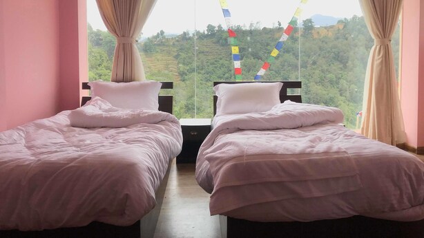 Una habitación con dos camas, cortinas color beige y vista a un paisaje verde por la ventana.