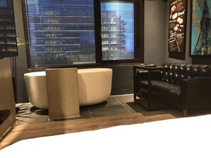 A modern bathroom with a large bathtub, a black leather sofa, and a cityscape view through the windows. - PInHouse (Kaohsiung)