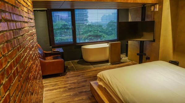 A modern bathroom with a bathtub, a shower area, and a toilet. There is a window providing natural light and a view of greenery outside. - PInHouse (Kaohsiung)