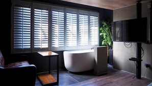 A modern bathroom with a bathtub, a large window with blinds, a television, and a potted plant. - PInHouse (Kaohsiung)