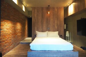 A modern bedroom with a brick wall, a wooden panel wall, a large bed, a TV, and a small table. - PInHouse (Kaohsiung)