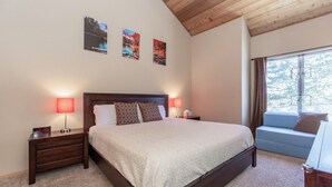 A bedroom with a large bed, two bedside tables with lamps, a window with curtains, and three framed pictures on the wall. - Condo with Mountain Views! Shared Hot Tub! Shuttle Access! (Mammoth Lakes)