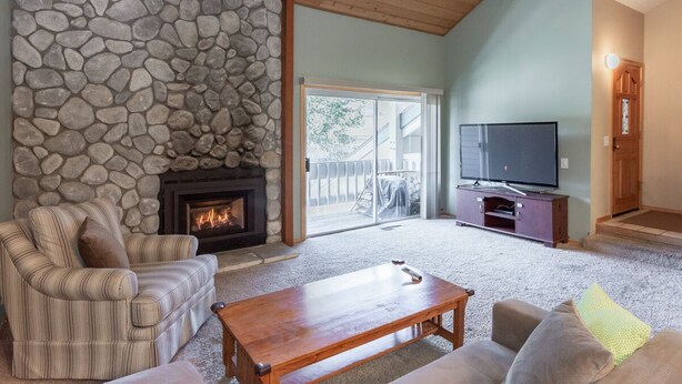 A living room with a stone fireplace, a television, and a sofa. - Condo with Mountain Views! Shared Hot Tub! Shuttle Access! (Mammoth Lakes)