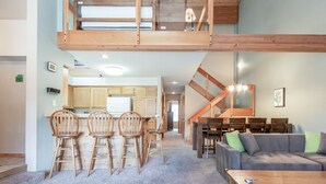 A spacious living area with a high ceiling, wooden furniture, and a staircase leading to an upper level. - Condo with Mountain Views! Shared Hot Tub! Shuttle Access! (Mammoth Lakes)