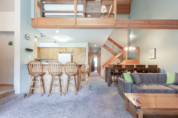 A spacious living area with a high ceiling, wooden furniture, and a staircase leading to an upper level.