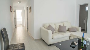 Una sala de estar moderna con un sofá y una mesa de centro, un pasillo que conduce a otra habitación y una puerta a la derecha.