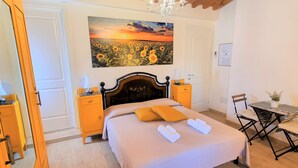 Een slaapkamer met een bed, een kroonluchter, een schilderij van zonnebloemen, een houten plafond en een klein tafeltje met stoelen.