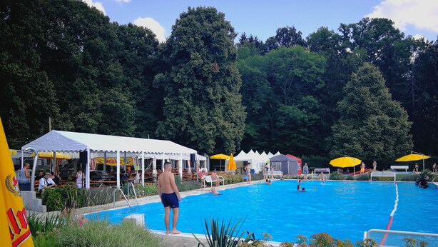 Zona de piscina con un área de estar cubierta y sombrillas.