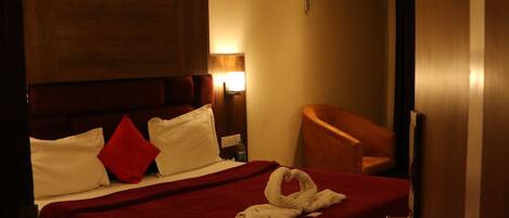 Quarto de hotel com uma cama grande, cabeceira de madeira, manta vermelha e ventoinha no teto.