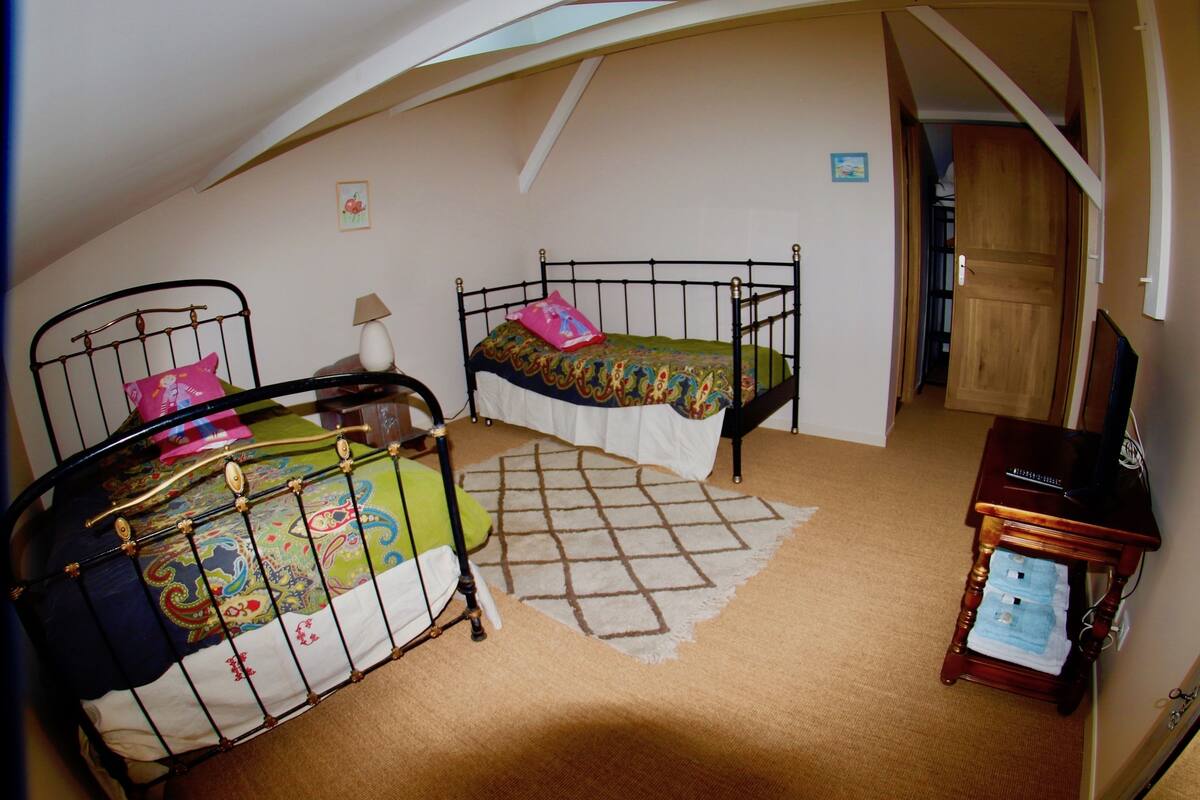 Ein Schlafzimmer mit zwei Einzelbetten, einem Holztisch mit Stuhl, einer Lampe und einem kleinen Teppich.