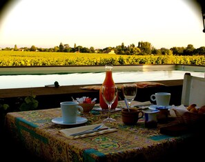 A table set with a white cup, a glass, a bottle, and a bowl, overlooking a field and water. - Chateau Trillon (Sauternes)