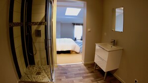 Une chambre d’hôtel avec une douche, un lit, une table de chevet, un miroir et un plancher en bois.