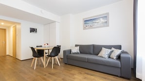 Ein modernes Wohnzimmer mit grauem Sofa, schwarzen Stühlen, einem Holzessttisch und einem Gemälde an der Wand.