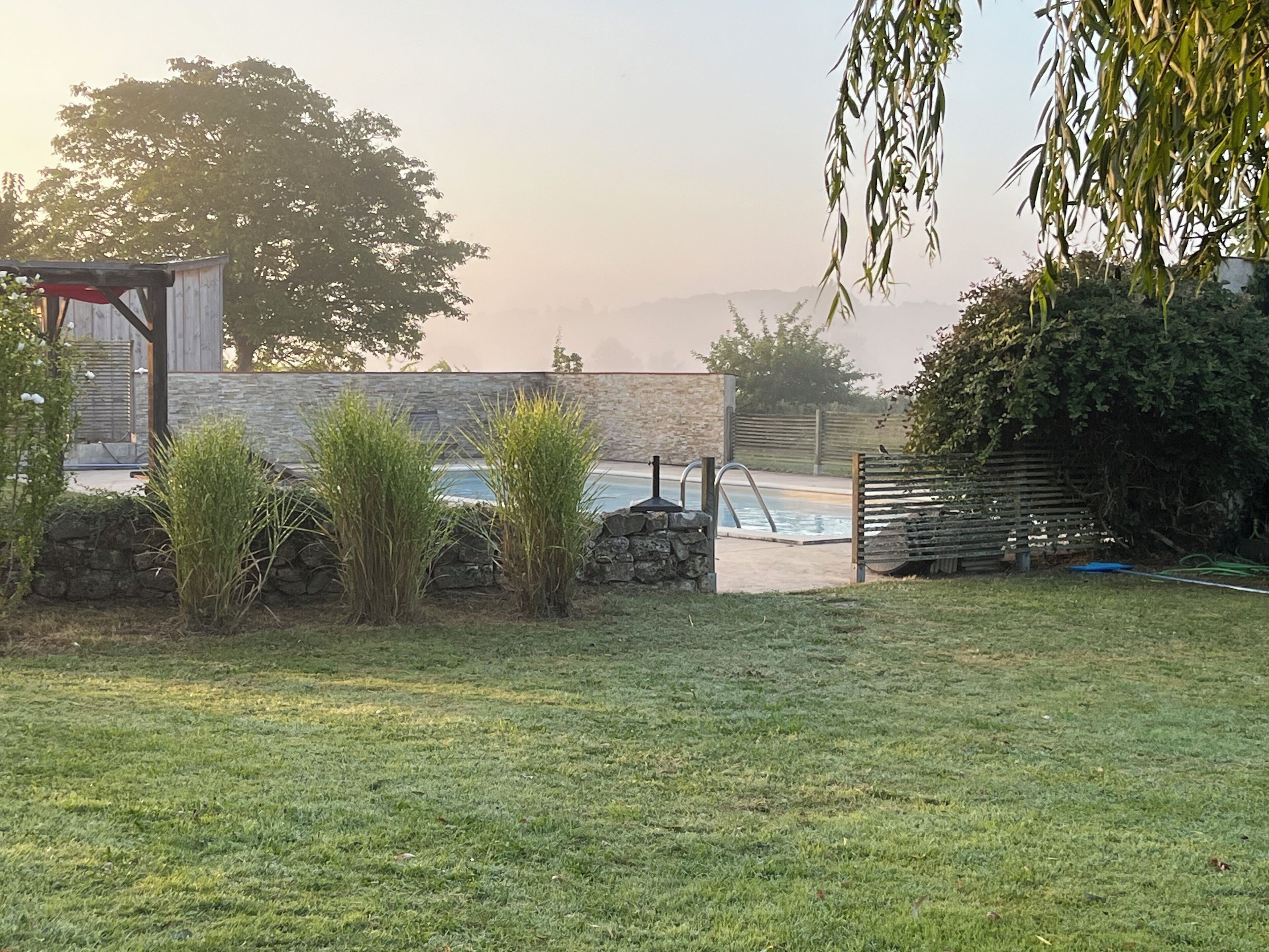 A backyard with a pool, stone wall, and a wooden structure.