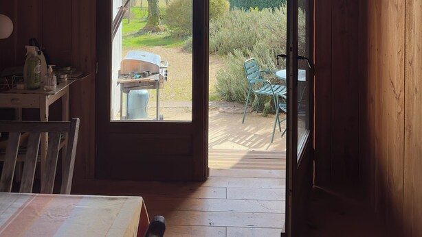 A wooden room with a large sliding glass door leading to an outdoor patio with a table and chairs. - Les Foucauds. A little paradise among the vines (Saint-Quentin-de-Caplong)