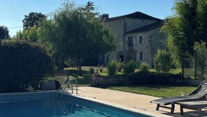 A swimming pool with lounge chairs, a stone building, and a clear blue sky. - Les Foucauds. A little paradise among the vines (Saint-Quentin-de-Caplong)