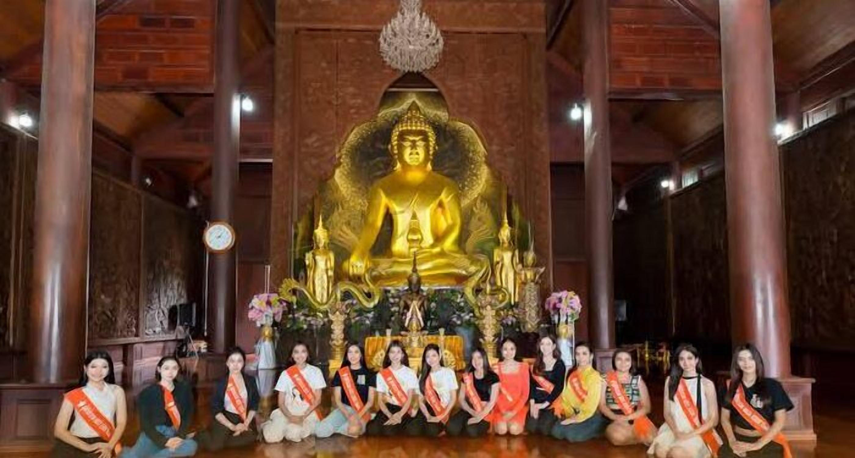 A group of people seated in front of a large golden Buddha statue in a temple setting.