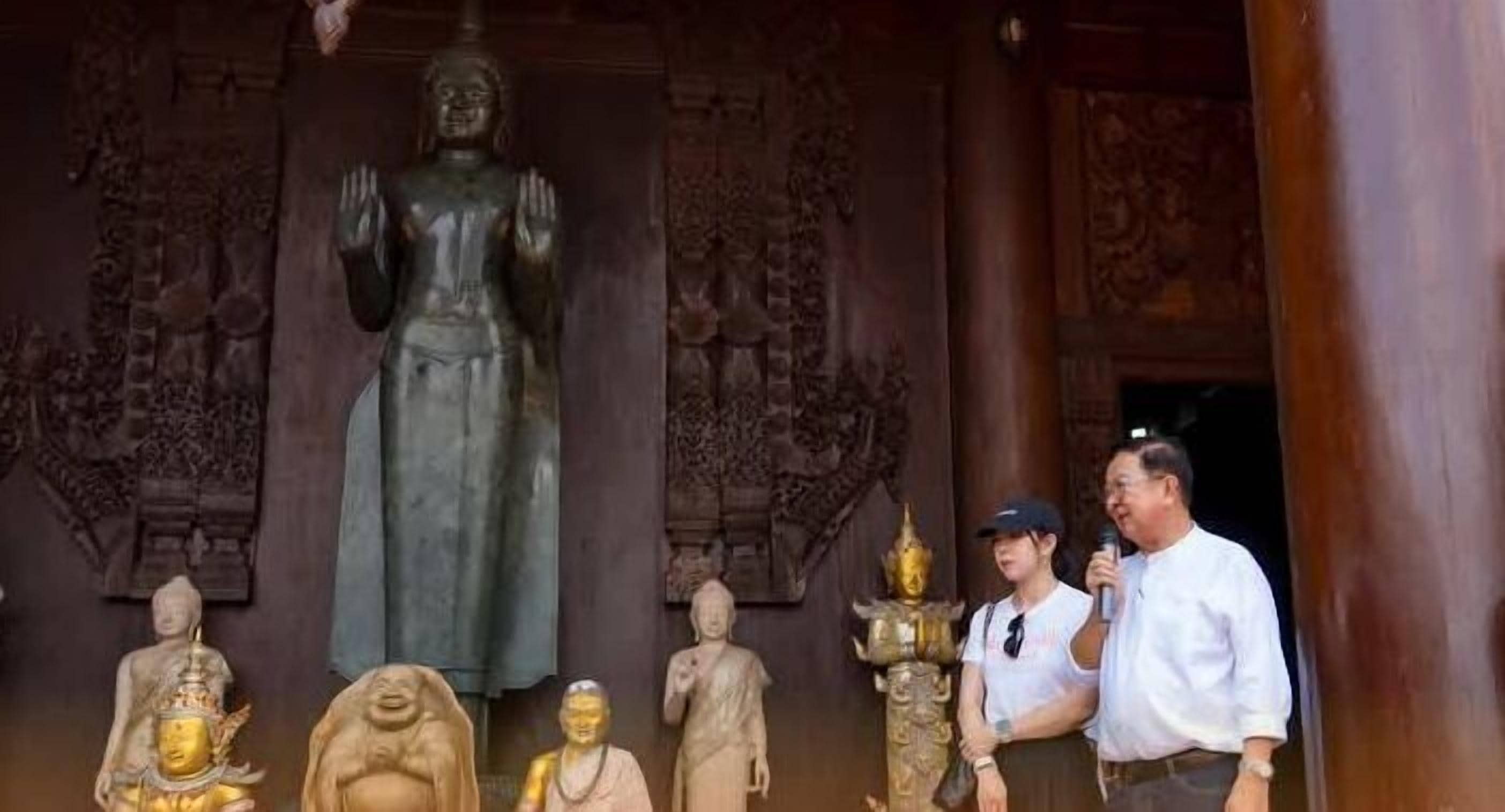 A large Buddha statue in a temple setting with intricate carvings on the walls.