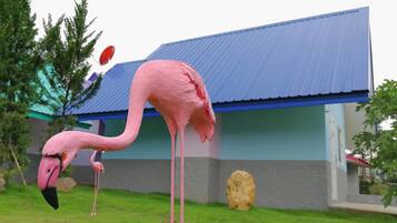 A pink flamingo in a grassy area with a building in the background.