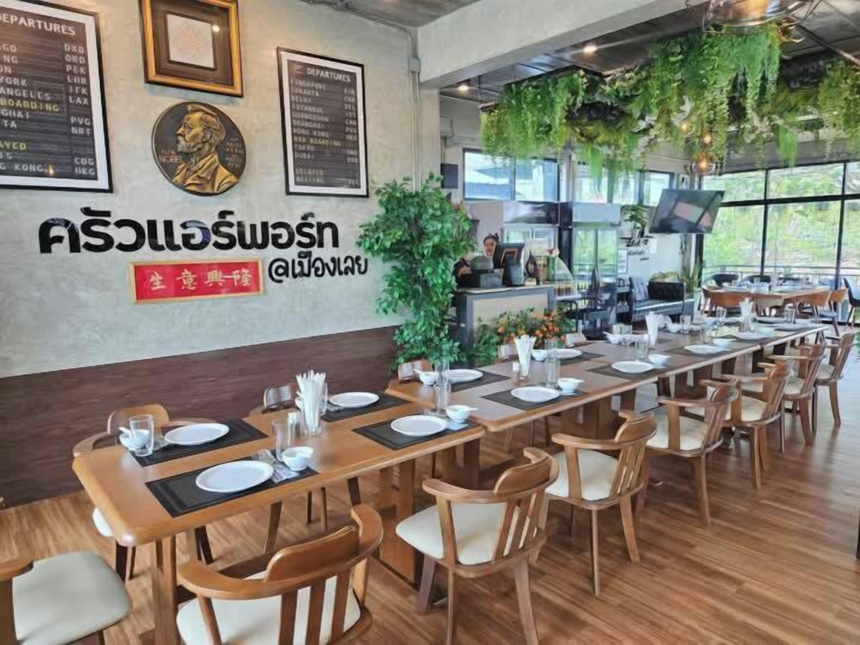 A restaurant with a long wooden table set for dining, a menu board on the wall, and a large window with a view.