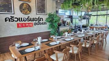 A restaurant with a long wooden table set for dining, a menu board on the wall, and a large window with a view.