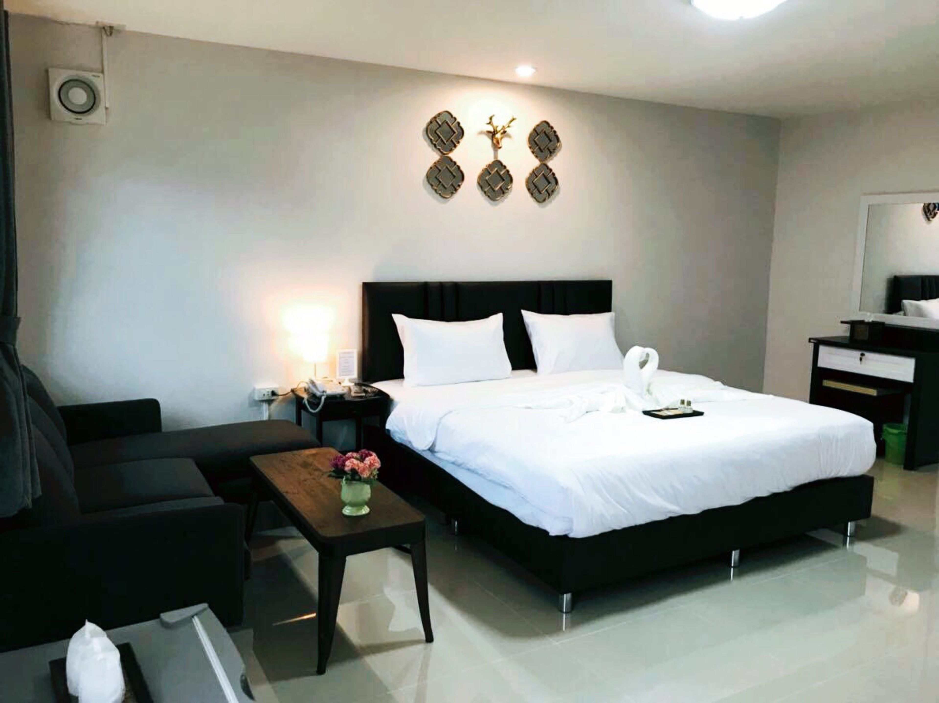Una habitación de hotel moderna con una cama grande, una mesita de noche con un florero, un escritorio, una silla y un aire acondicionado instalado en la pared.