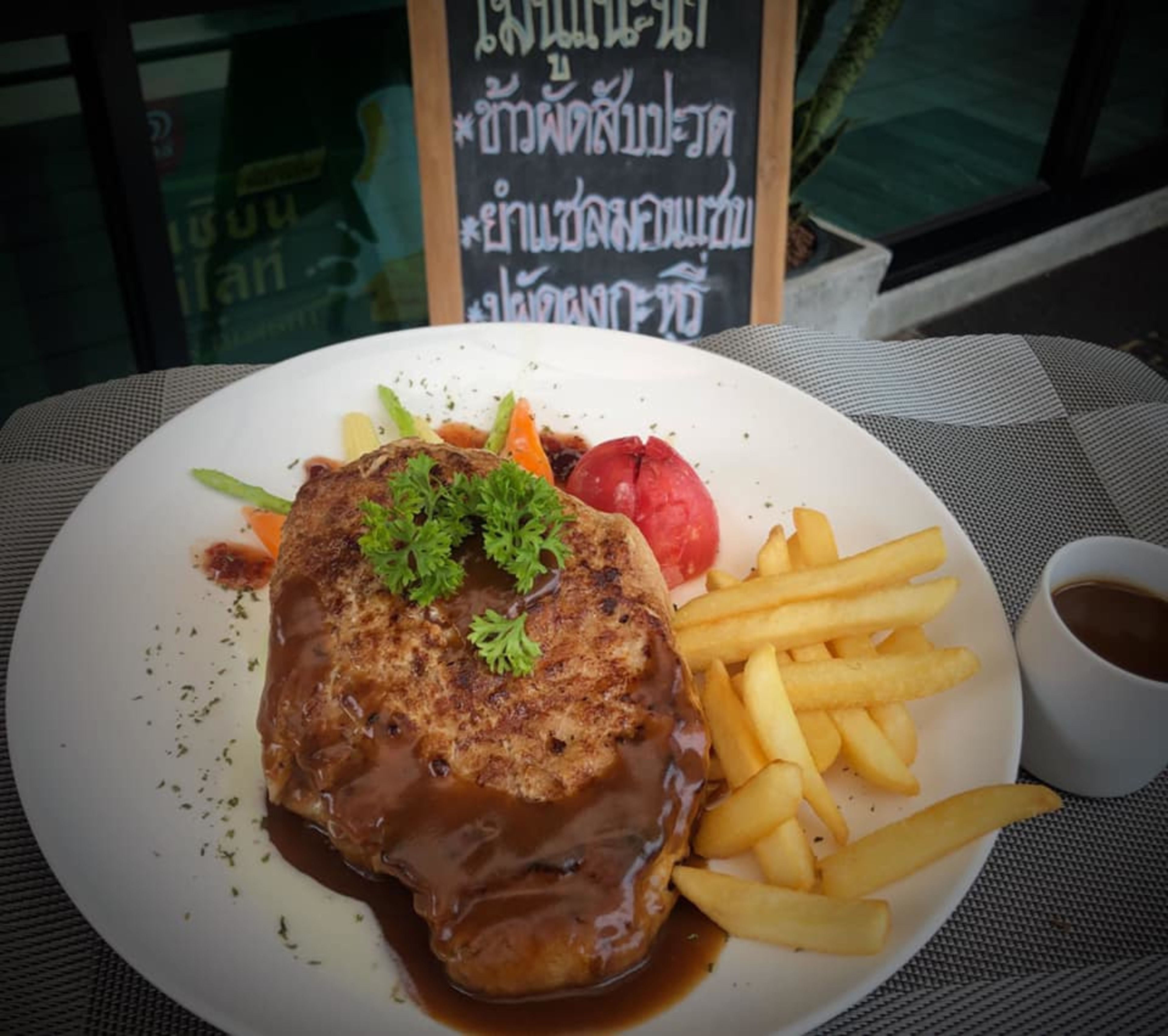 A plate with a steak, fries, and a red fruit, served on a table with a menu in the background.