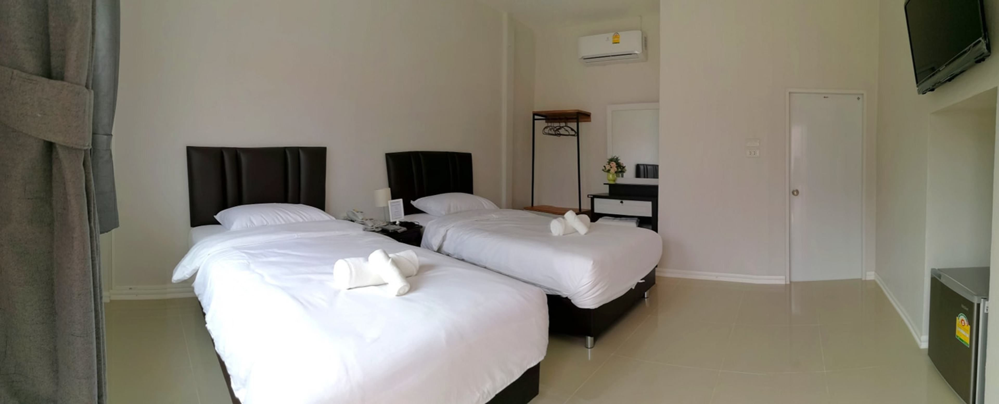 Habitación de hotel con dos camas, una mesita de noche con lámpara, un pequeño escritorio con silla, un armario y un televisor montado en la pared.