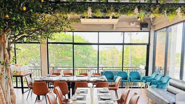 A modern dining area with long tables, brown leather chairs, and a view of greenery through large windows. - Muang Loei Airport Hotel (Mueang Loei)