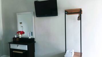 Quarto com cômoda de madeira escura, vaso branco com flores vermelhas, TV de tela plana na parede e um banco de madeira com toalha.