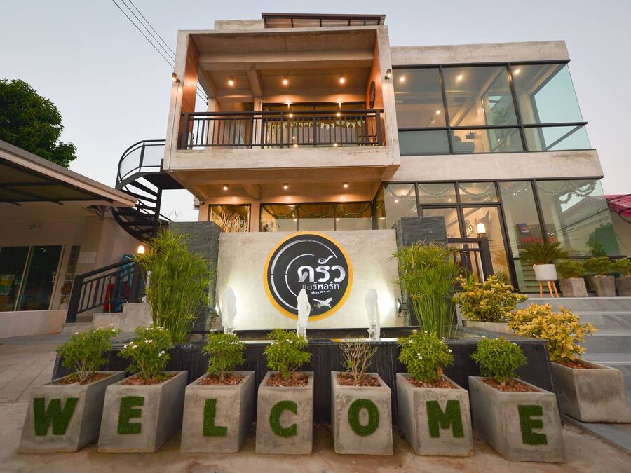 A modern building with a balcony, a welcome sign, and potted plants.