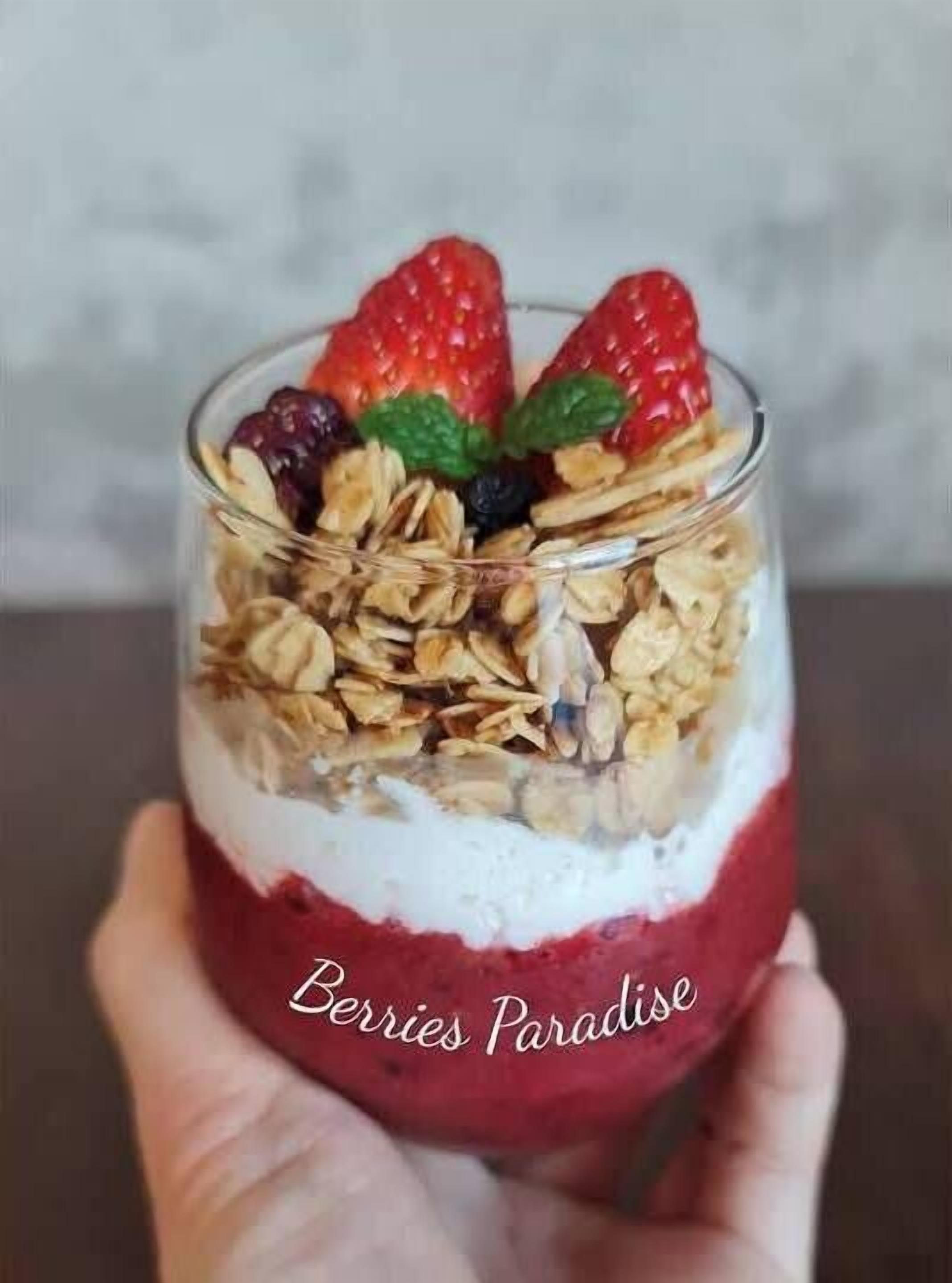 A layered dessert in a clear glass, with strawberries and granola visible.